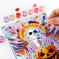 Person painting a colorful vintage metal poster with paint by numbers, featuring a skeleton and pumpkin design.