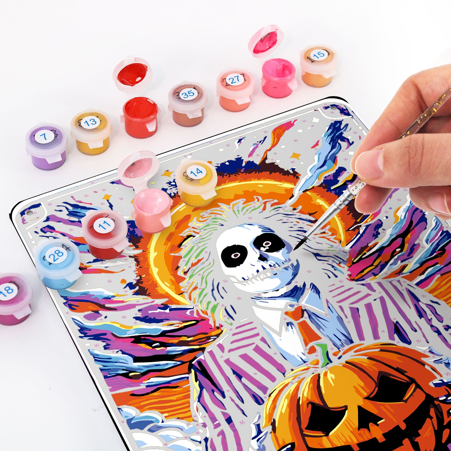 Person painting a colorful vintage metal poster with paint by numbers, featuring a skeleton and pumpkin design.